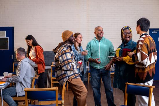 A group of people at a community centre, standing in a circle and talking to each other.