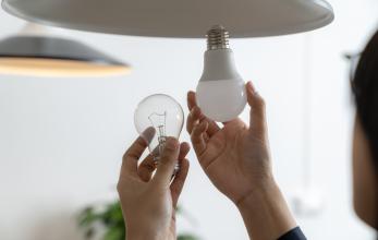 A person changing a light bulb from an incandescent bulb to an LED bulb.