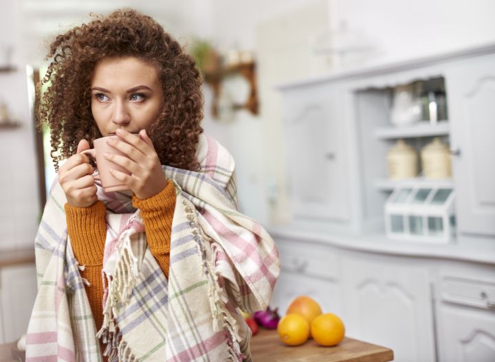 young woman wrapped in a blanket holding a warm drink
