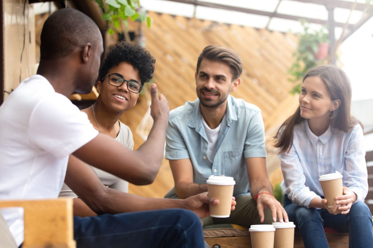 man giving a thumbs up to his friends as they sit drinking coffee in cafe