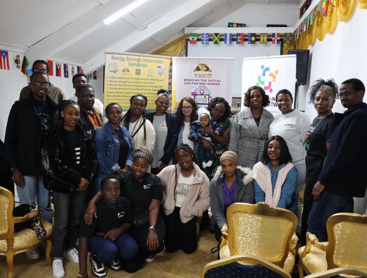 A group of people pose for a photo in a decorated room with flags, chairs, and banners promoting energy saving and digital literacy.