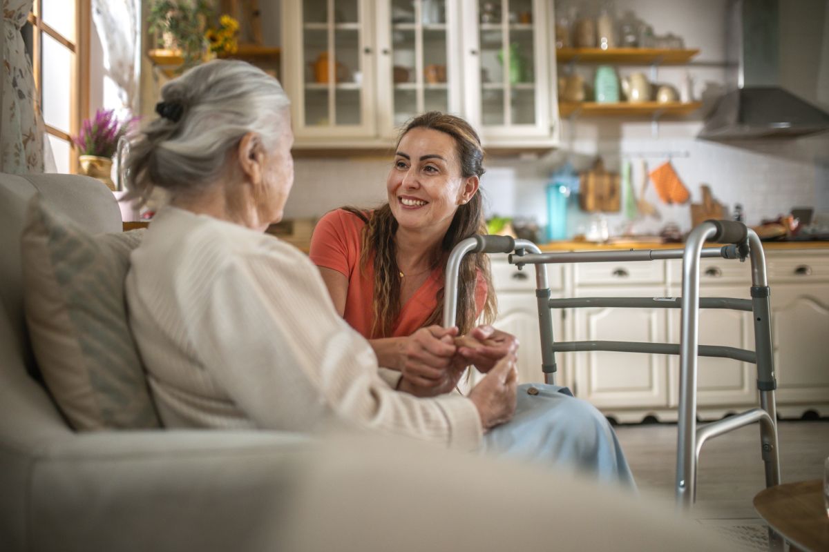 smiling young woman assisting a senior woman with a walking frame at home