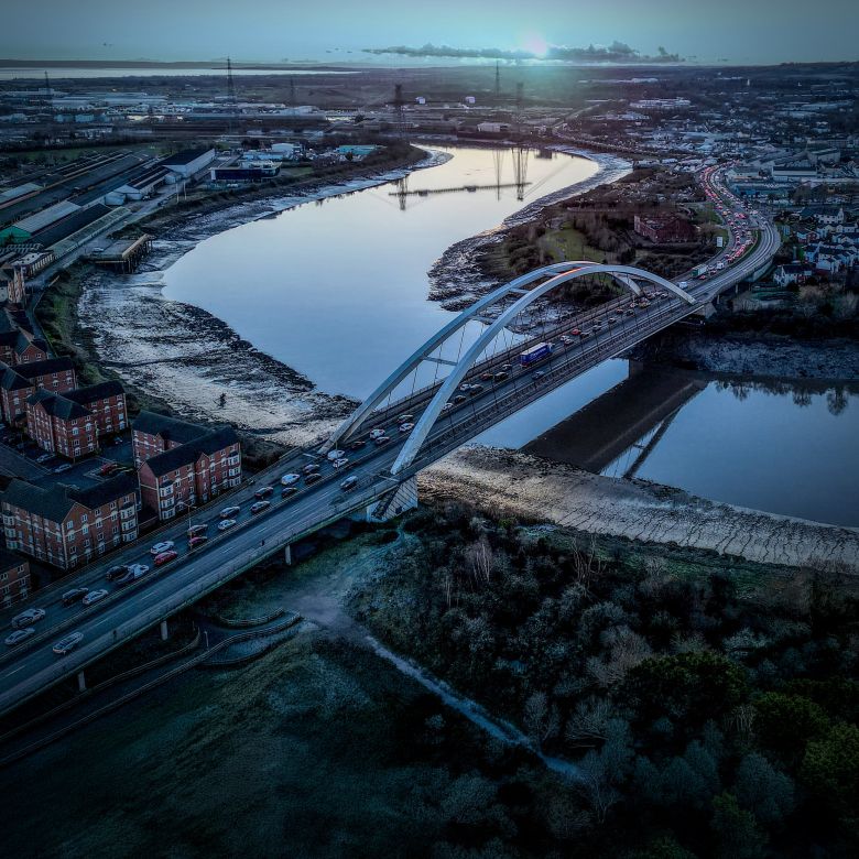 aerial view of a river winding through Newport as the sun sets, with a bridge and the sky reflected in the water
