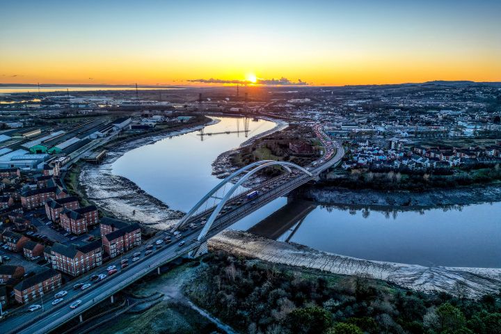 aerial view of a river winding through Newport as the sun sets, with a bridge and the sky reflected in the water