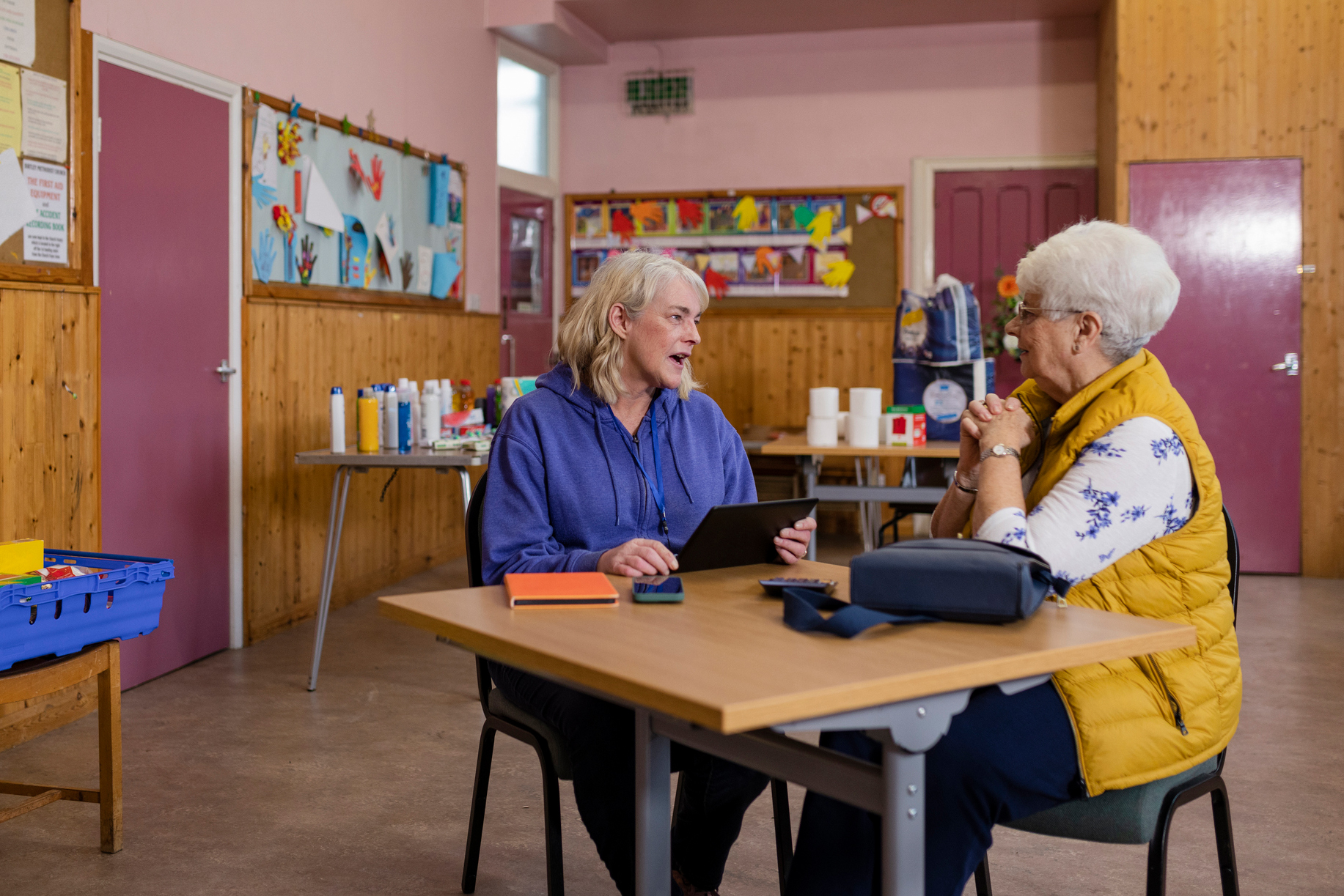 two older women sitting at a table together in a bright community space