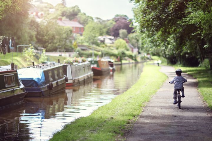young child riding a bike down a canal tow path with trees overhead on a sunny day