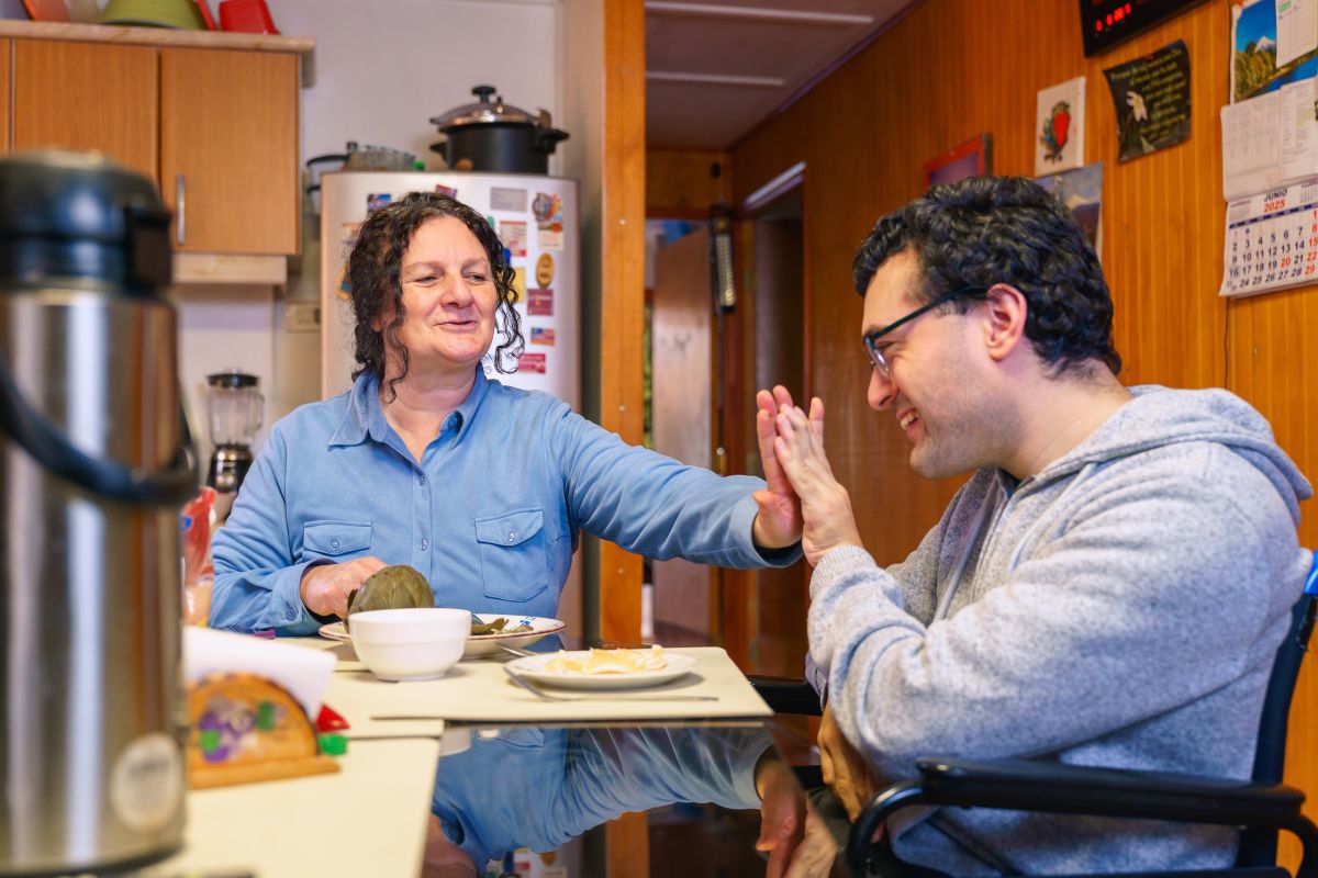 a woman and a young man with cerebral palsy sharing a high-five during a meal at home