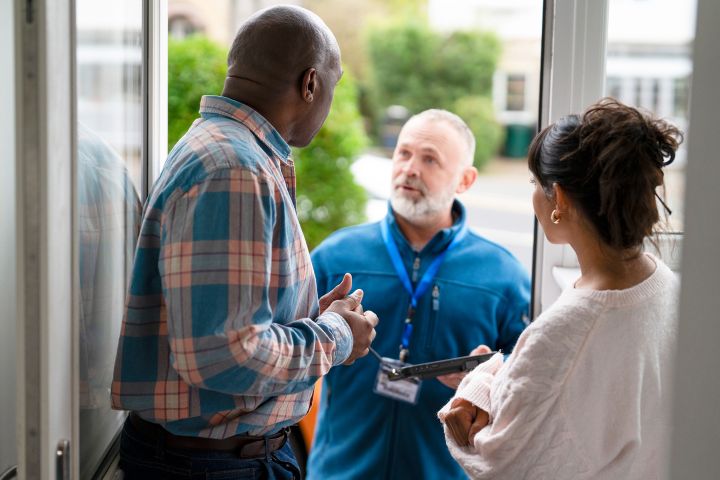 a service representative is speaking to two residents at their home, providing assistance and answering questions during a clear daytime