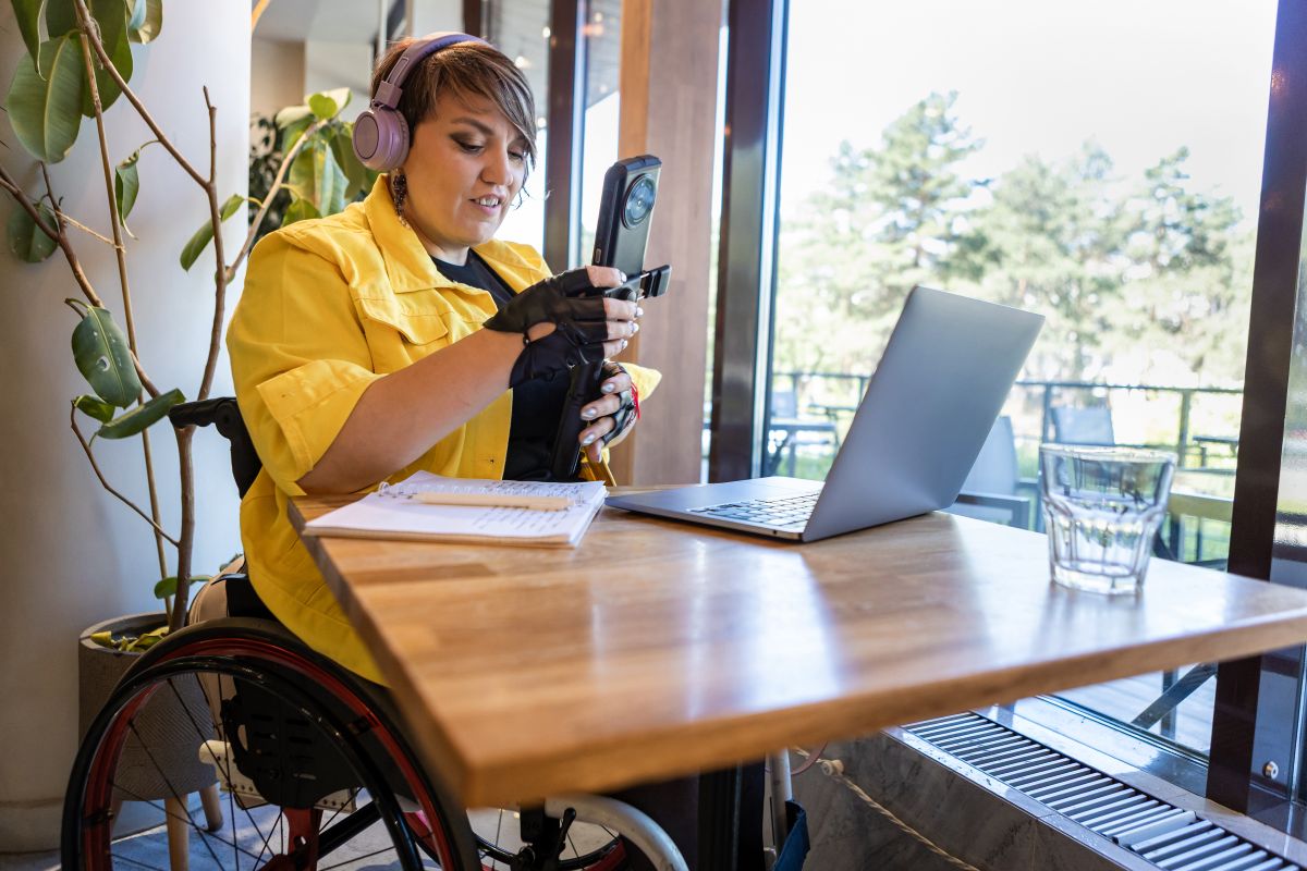 adult woman in a wheelchair smiles while taking notes near laptop and smartphone at a desk